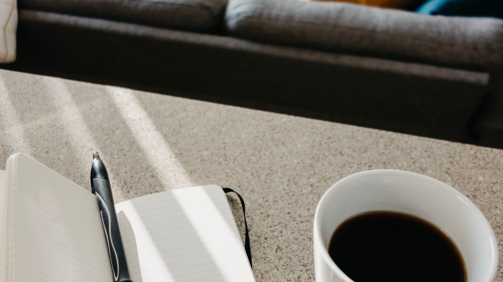 An open notebook and pen beside a cup of coffee