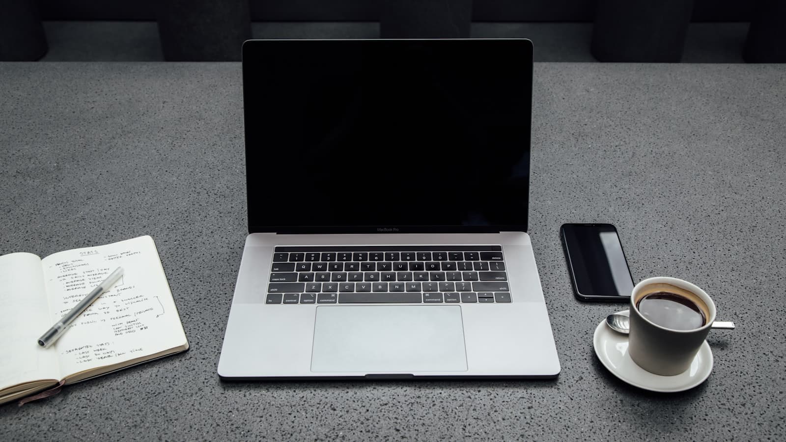 A laptop, notebook and pen on a desk during a planning session